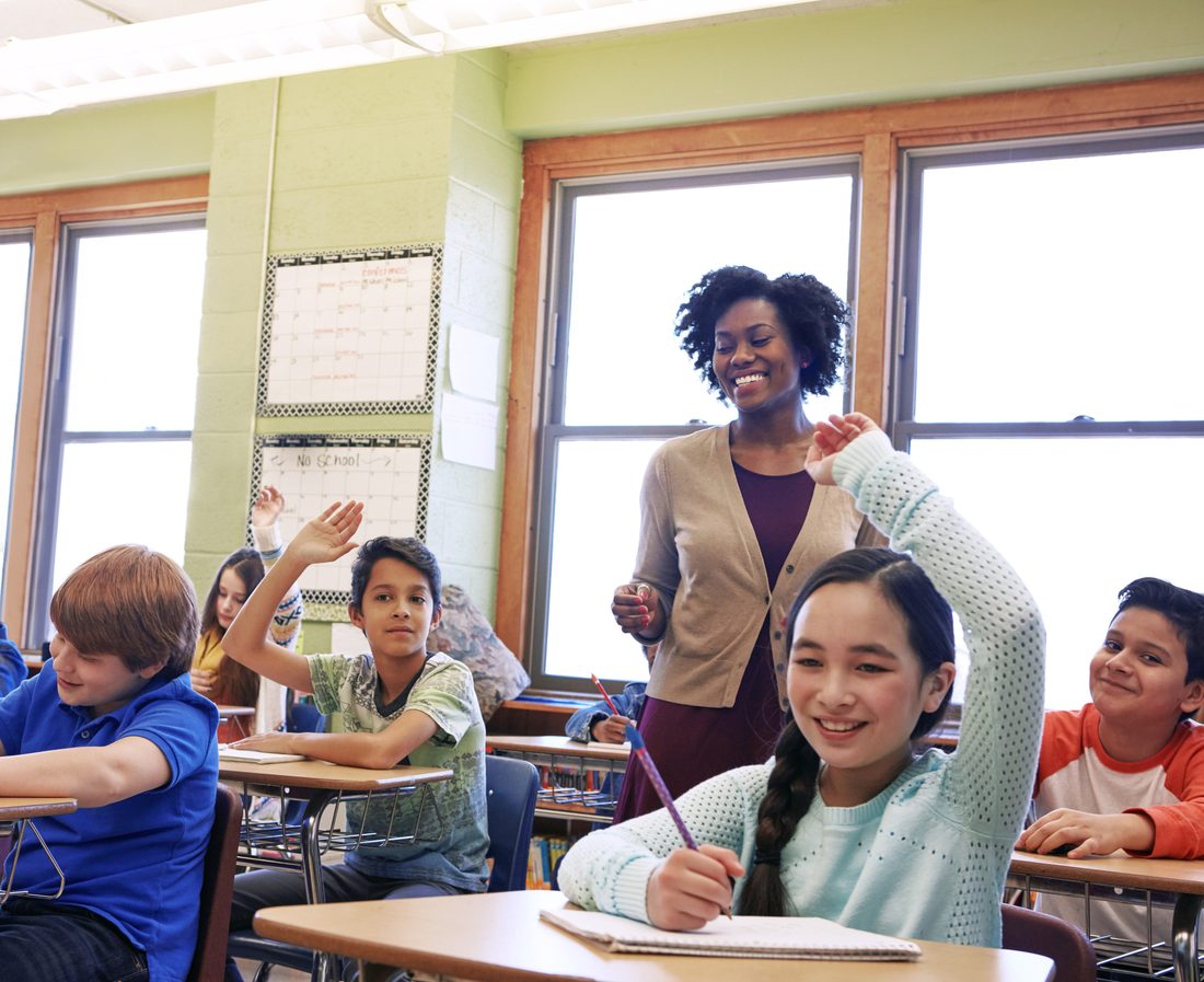 Elementary school children raising their hands to answer a question in class