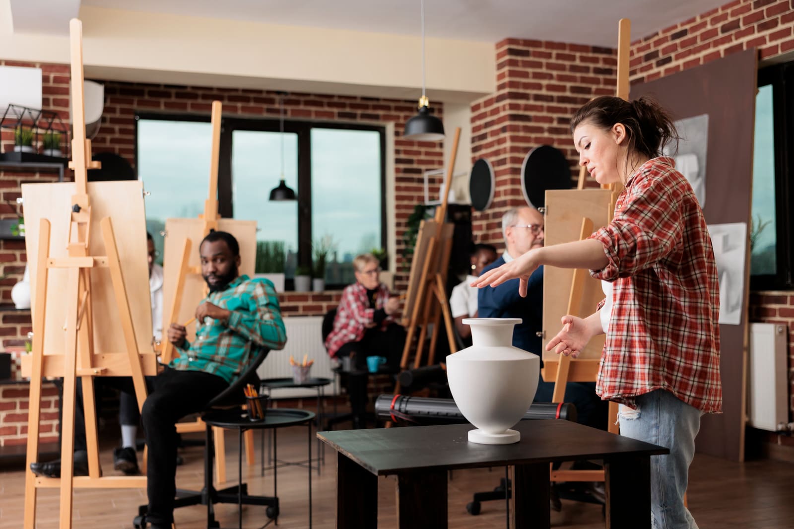 An art teacher helping a student at an easel in a bright studio classroom