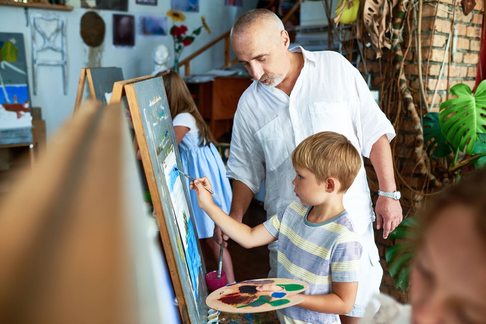 An art teacher helping a student at an easel in a bright studio classroom