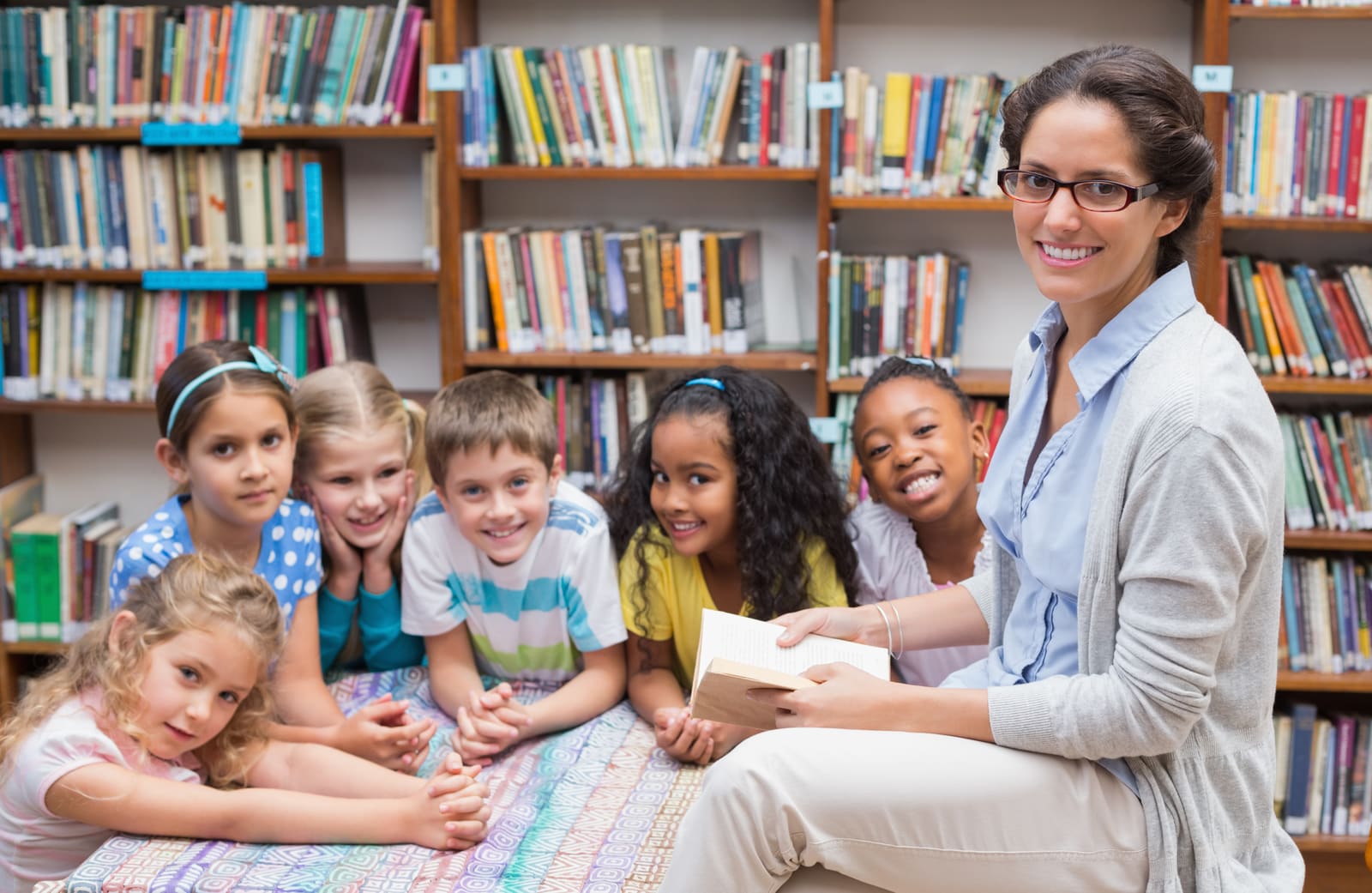 An English language arts teacher holding books among the shelves of a school library