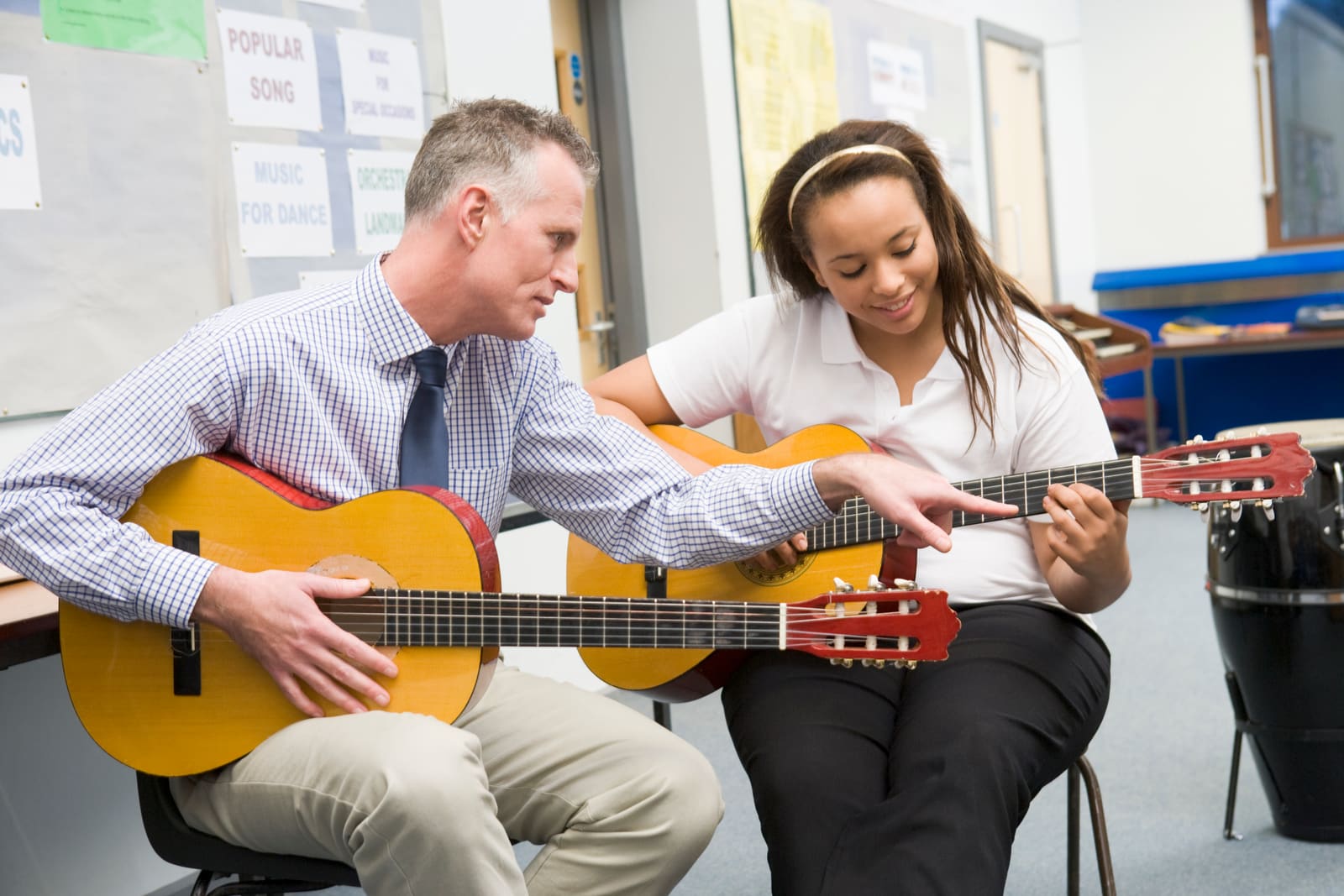 A music education teacher guiding a student reading sheet music at a keyboard