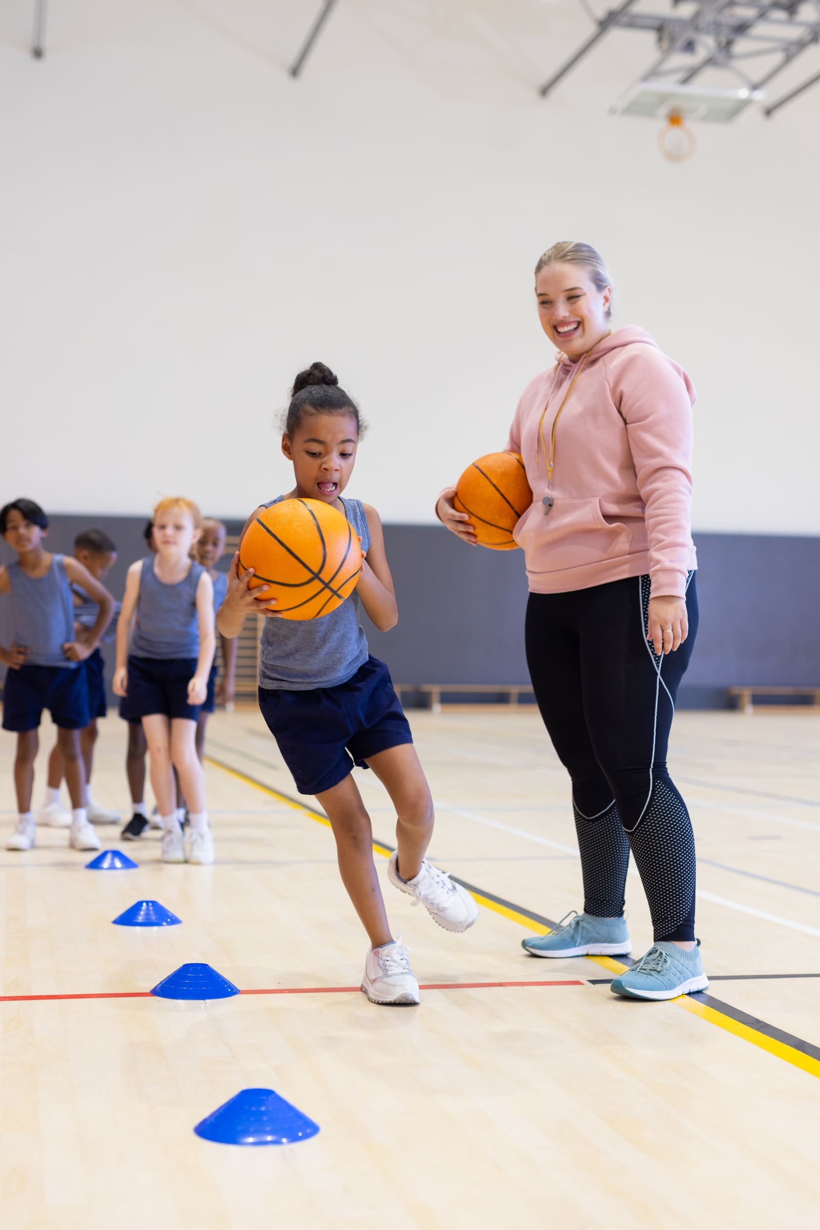 A physical education teacher leading elementary students through a ball drill in the school gym