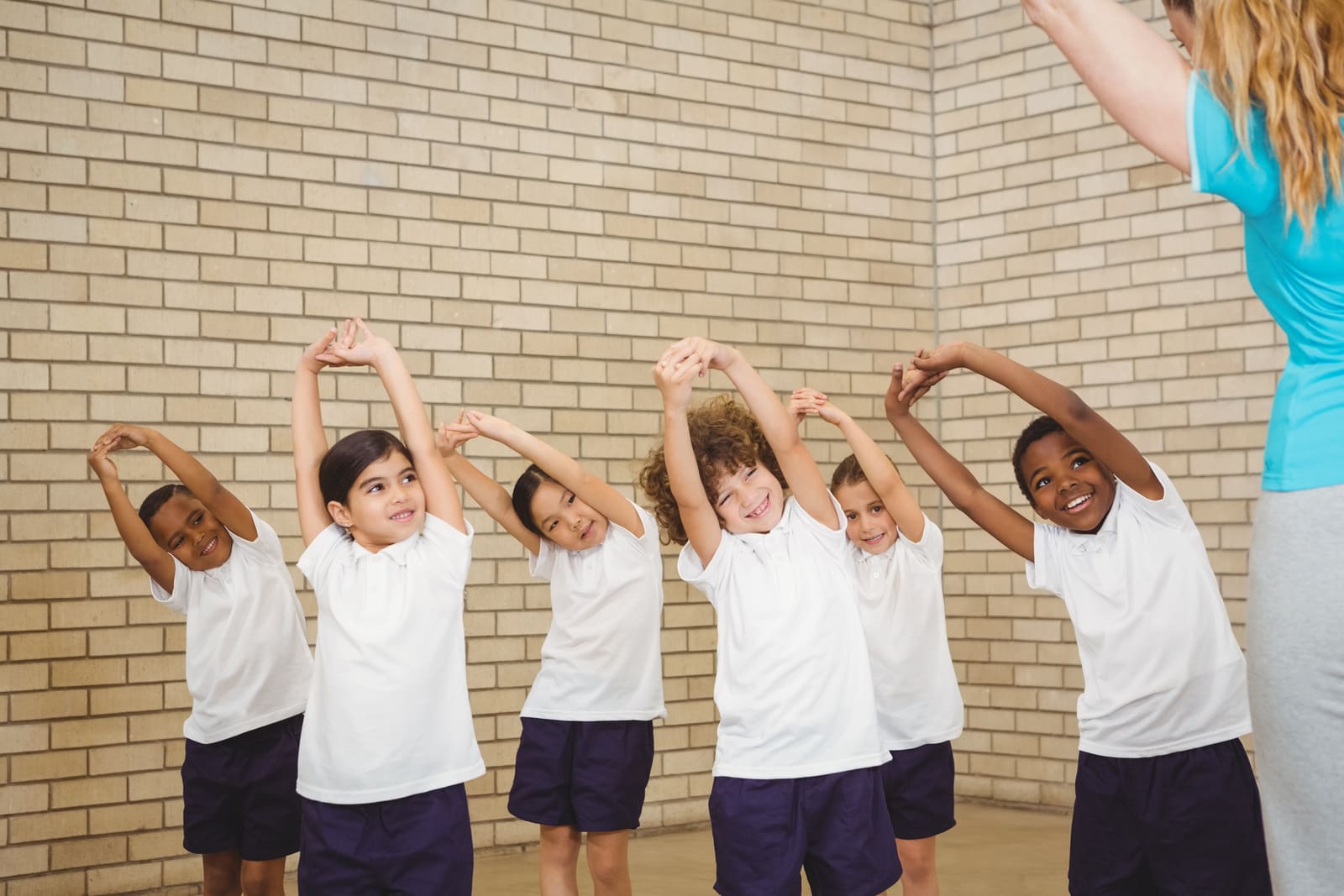 A physical education teacher leading elementary students through a ball drill in the school gym
