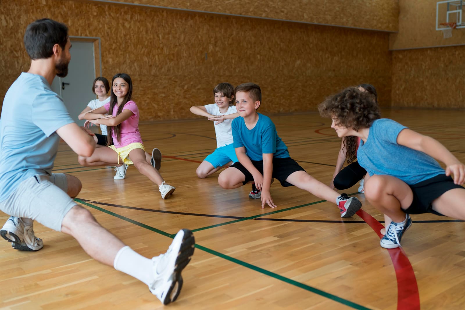 A physical education teacher leading elementary students through a ball drill in the school gym