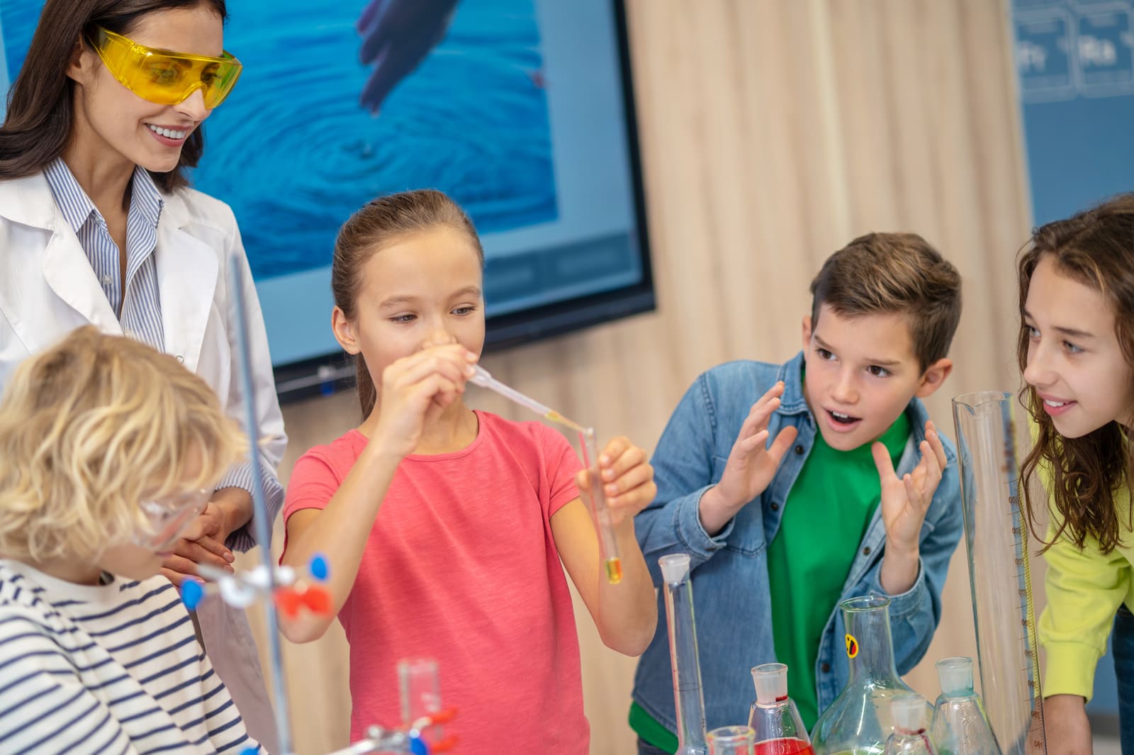 A science teacher guiding students through a hands-on experiment at a classroom lab bench