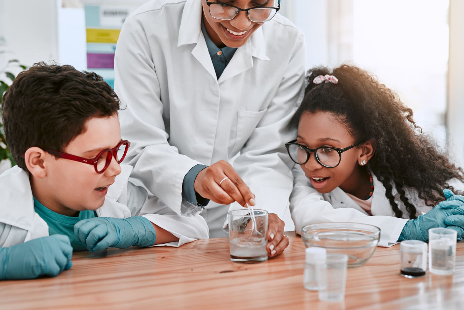 A science teacher guiding students through a hands-on experiment at a classroom lab bench