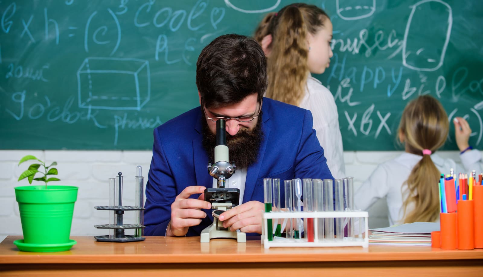 A biology teacher helping students examine specimens under microscopes in the lab